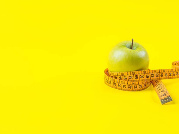 istock Green apple with measuring tape on yellow 1221642098