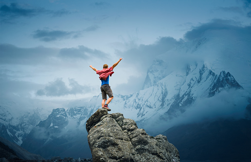 Young man standing with arms raised on top of the mountain in beautiful mountain scenery