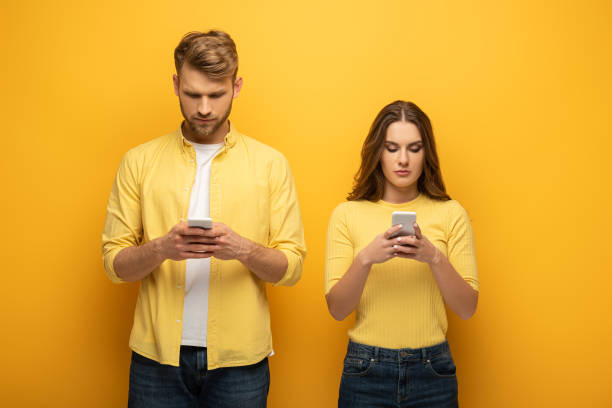 istock Young couple using smartphones on yellow background 1221651731