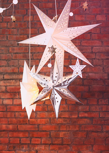 White decorative Christmas stars of various sizes and shapes hanging against red brick background