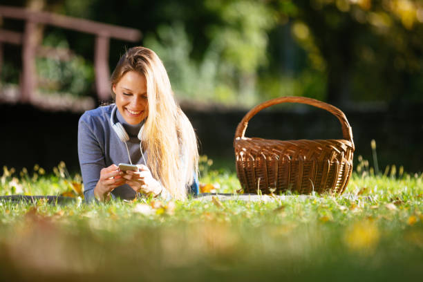 istock Smiling woman lying in grass and text messaging 1221658380