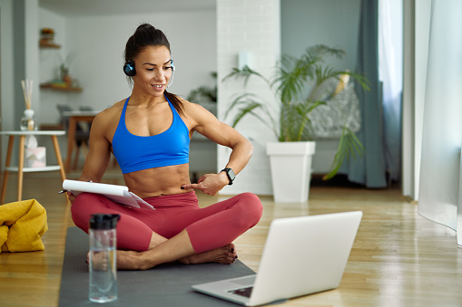 Female personal trainer using computer while holding online exercise class with her clients from home.