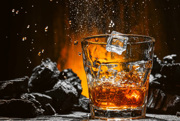 whiskey is poured into a glass ice falls into a glass with expensive whiskey and spray flies in different directions bourbon whiskey photos stock pictures, royalty-free photos & images