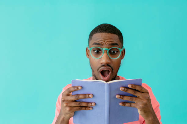 retrato de un joven sorprendido por lo que está leyendo libro, aislado en el espacio de copia azul - twist baile fotografías e imágenes de stock