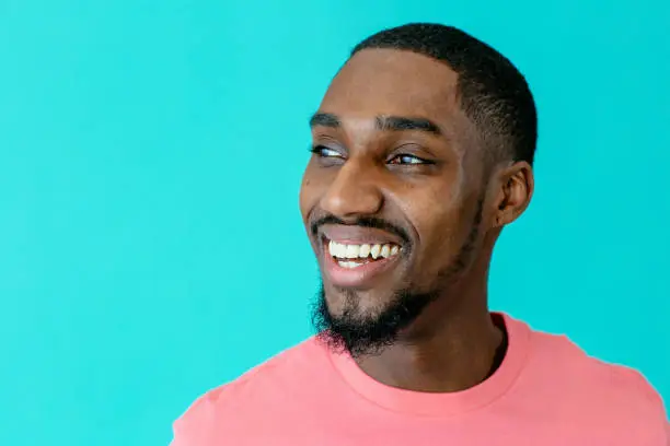 Portrait of a happy young man smiling and looking up to side, against blue studio background