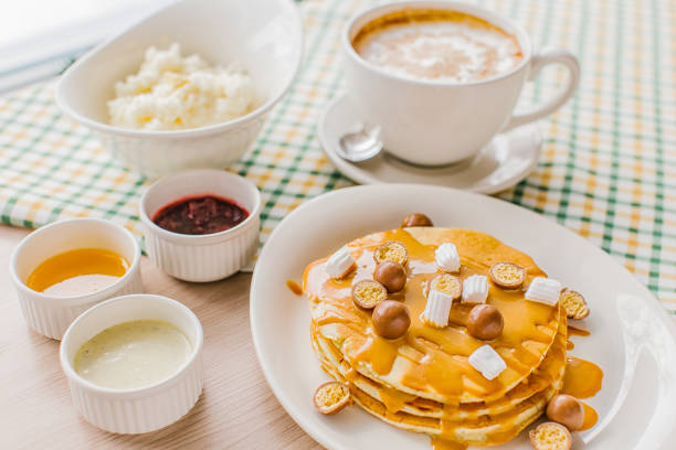 angle view of a breakfast table with a plate of pancakes with caramel, maltesers and marshmallows. On a background of latte and rice porridge