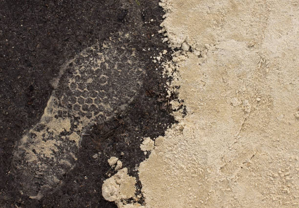 A sandy boot print on the ground next to a pile of sand.