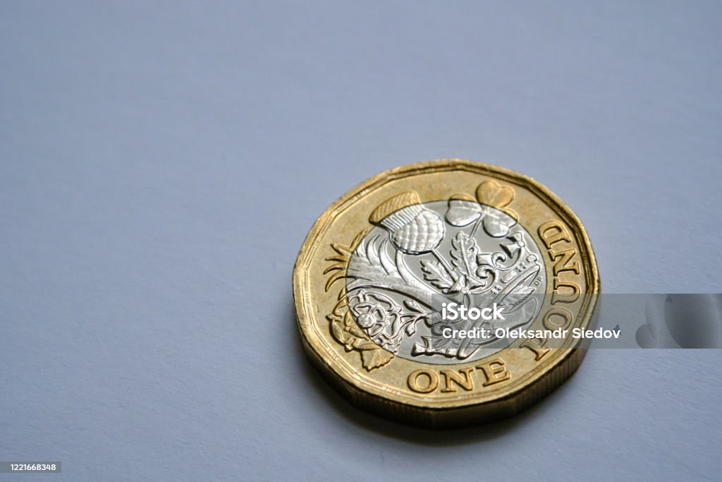 One pound coin close up photo with selective focus and dramatic shadow. British One pound coin isolated on white paper with hard shadows. Illustrative for personal finance, money saving and pound sterling inflation. Coin Stock Photo