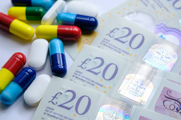 Pile of different colourful pills placed next to 20 British pound banknotes. stock photo