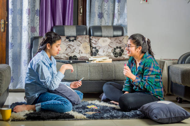 two girls sitting at home playing with cards two girls sitting in room and playing cards for timepass family playing card game stock pictures, royalty-free photos & images