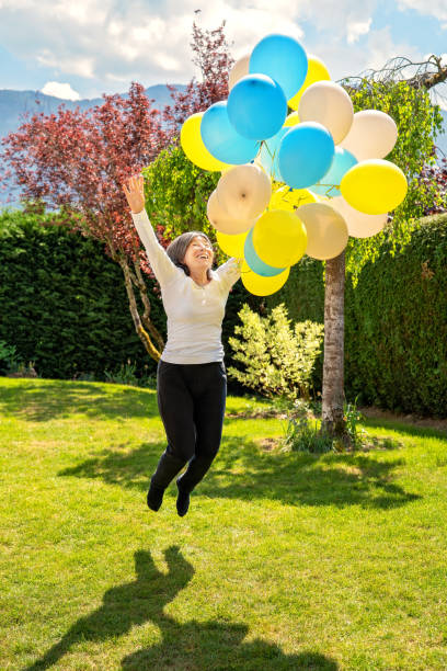 glücklich aufgeregt senior 65 jahre alte frau hält bunte luftballons springen und fliegen in der luft in ihrem garten. pures glück. aktives senior lifestyle konzept. - 60 65 years stock-fotos und bilder