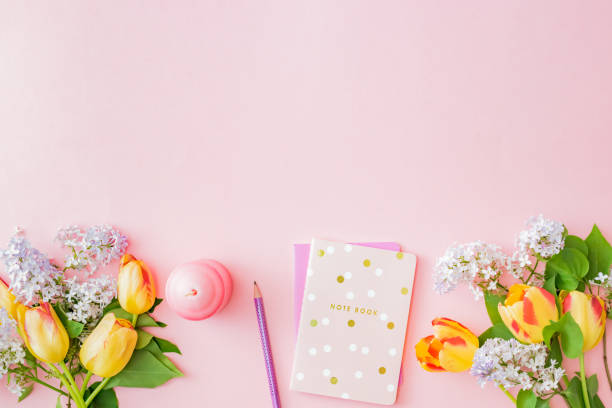 istock Flat lay blogger or freelancer workspace with a notebook and yellow tulips branches of lilac on a pink background 1221676782