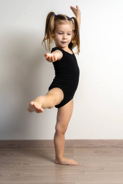 little girl 3-4 years old in a black gymnastics leotard raises her leg and arm. children sport - child caucasian little girls 3 4 years imagens e fotografias de stock