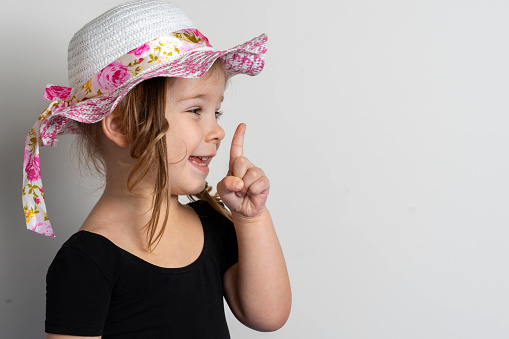 little European girl on a light background in a summer hat raised her finger up and laughs. the birth of an idea