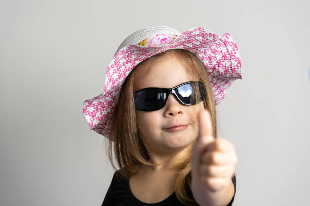 a cheerful little girl of 3-4 years old in sunglasses and a summer hat smiles happily and grimaces - child caucasian little girls 3 4 years imagens e fotografias de stock