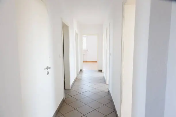 Corridor in appartment: unfurnished, with white walls, ground is covered with gray tiles, there are 7 doors visible