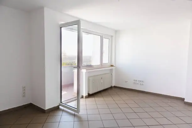 living room without furniture, there is a balcony, the door is open and ther is a great view over Ruhr valley at a sunny, walls are painted white