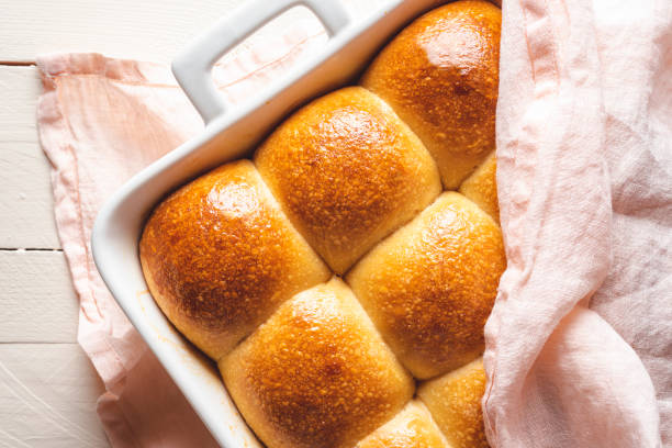 Bread buns freshly baked covered with a kitchen towel Top view with freshly baked bread in a ceramic oven tray. Bread buns baked in a white tray covered with a pink towel. Homemade bread with a delicious golden crust above view. bun stock pictures, royalty-free photos & images