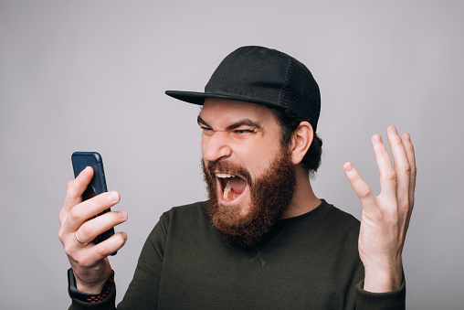 Screaming  bearded man is looking to his phone on white background.