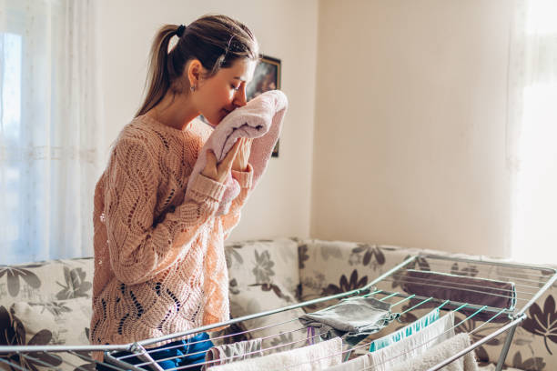 mulher feliz cheirando recolheu roupas limpas de secadora em pilha. limpeza e tarefas domésticas - faro - fotografias e filmes do acervo