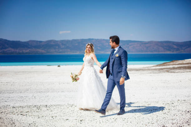 Bride and groom walking hand in hand on the white sandy beach.