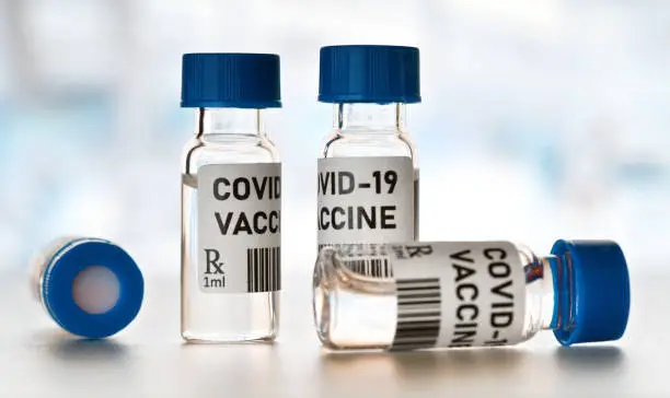 Photo of Coronavirus Covid-19 vaccine concept - small glass vials with blue caps on white table, closeup detail (own design - dummy bar code)