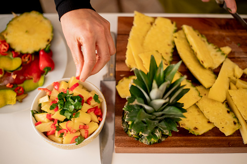 Unrecognisable mid-adult mixed-race woman making pineapple salsa.