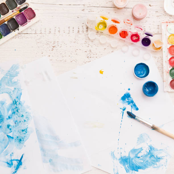 istock Directly above on paints and brushes on white wooden table background. Creative ideas, creativity and early learning. 1221695098
