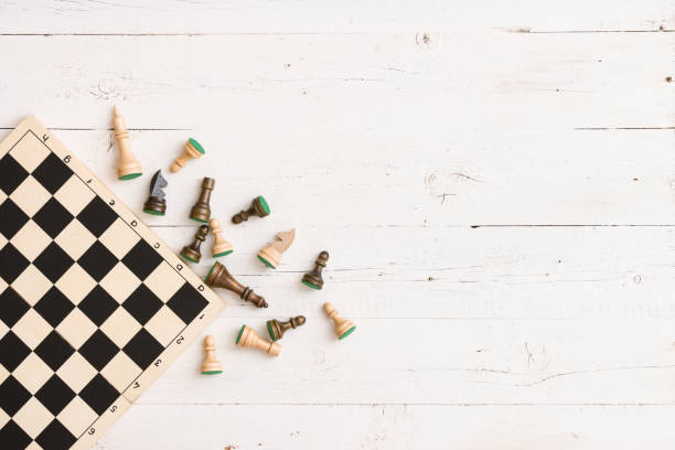 istock wooden chess figures and part of a chess board on white table background. Top view. 1221695149