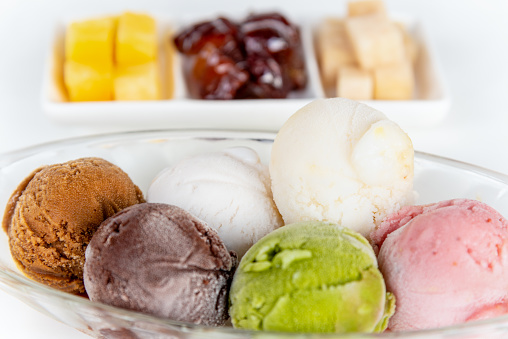 Closeup side view multi colored ice cream in a clear dish and sweet processed fruit for eating together in Thai style, Set of colorful ice cream scoops of different colors on the white table background