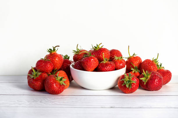 istock Fresh strawberries in white ceramic bowl on white wooden table 1221695862