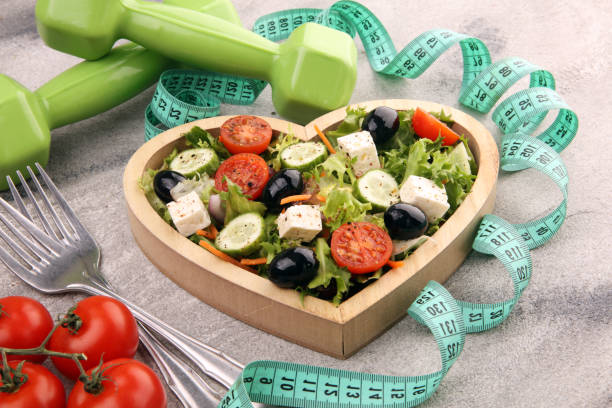 istock Authentic fresh salad in a wooden heart shaped cup with dumbbells excercise equipment, measuring tape on table. healthy lifestyles, good health 1221697190
