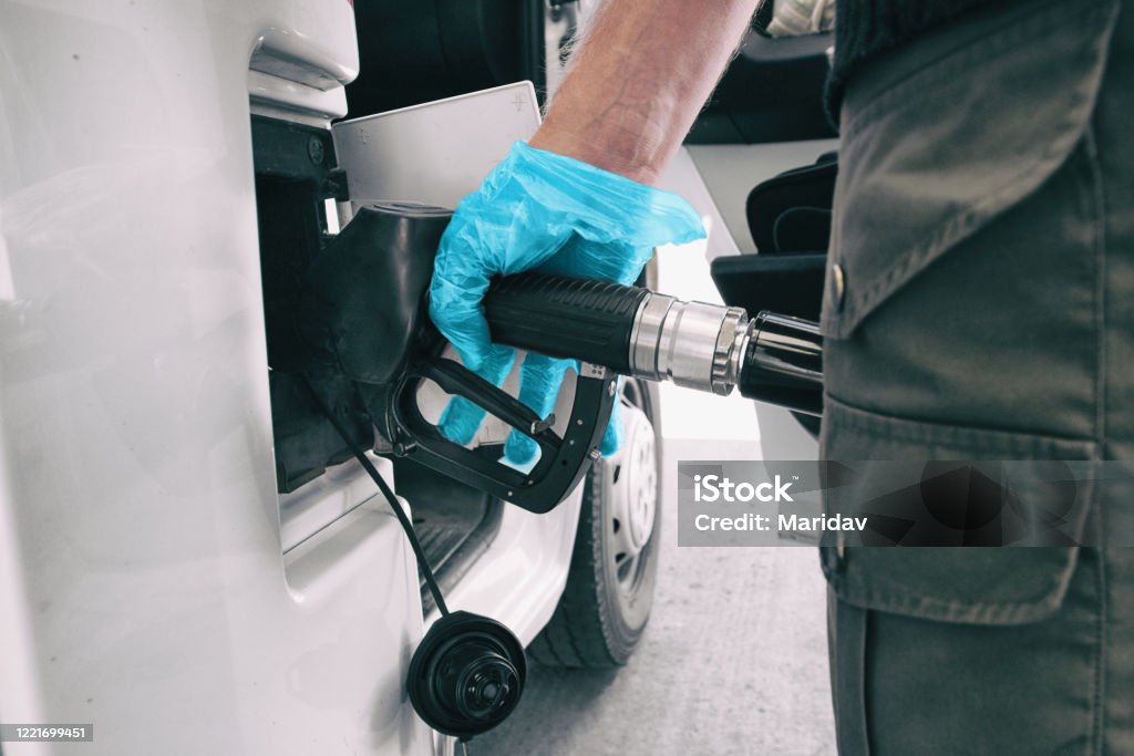 Los precios del gasóleo coronavirus caen al hombre bombeando gasolina en una gasolinera con guante azul médico como COVID-19 difundiendo protección de seguridad para tocar gérmenes - Foto de stock de Autocaravana libre de derechos