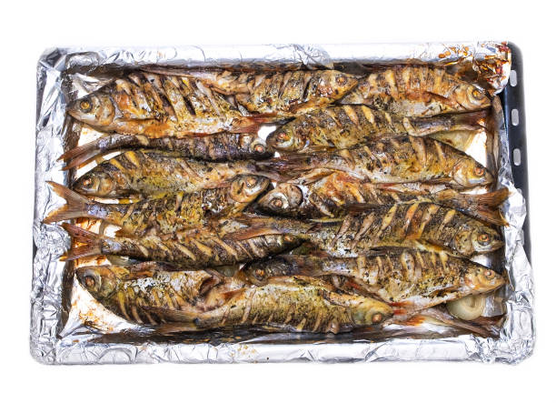 Roasted fish in the oven. The fish lies on a metal pan, view from the top. On a white isolated background Roasted fish in the oven. The fish lies on a metal pan, view from the top. On a white isolated background rudd fish stock pictures, royalty-free photos & images