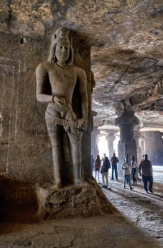 Massive stone carvings in a cave on an island in the Mumbai harbor. Visitors dwarfed by the scale of the figures.