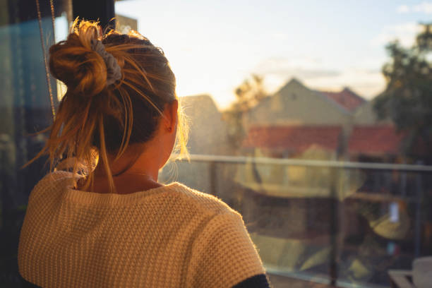 mujer mirando a través de la ventana al atardecer. - women depression window sadness fotografías e imágenes de stock