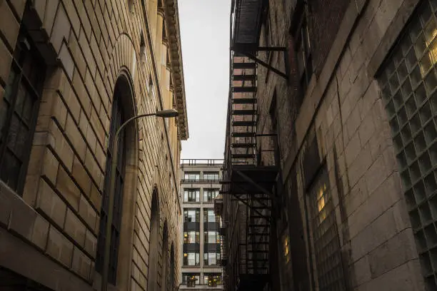 Photo of Fire escape stairs and ladder, in metal, on a typical North American old stone building from the Old Montreal, Quebec, Canada in a narrow and dark street.