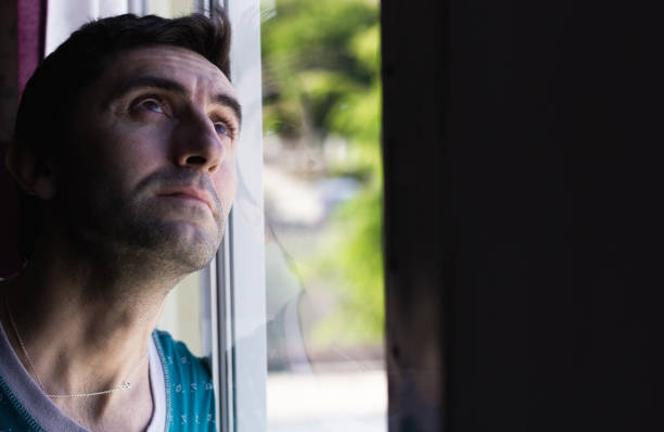 istock Young man looking up over window in dark room 1221706710