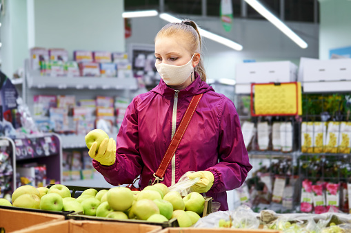 woman in homemade mask and protective gloves buys food in a store during a coronavirus COVID-19 pandemic