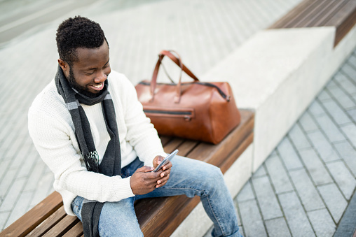 Smiling African American man using mobile phone outdoors in the city.