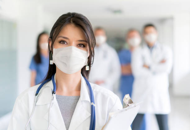 Doctor working at the hospital wearing a facemask to avoid COVID-19 Portrait of a female doctor working at the hospital wearing a facemask to avoid COVID-19 with staff at the background â Pandemic concepts n95 face mask photos stock pictures, royalty-free photos & images