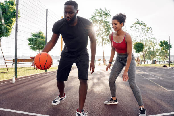 Outdoors Activity. African couple guy dribbling concentrated while girl defencing backdoor happy on basketball court