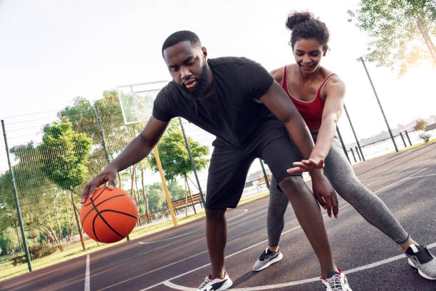 Outdoors Activity. African couple guy dribbling while girl defencing backdoor on basketball court smiling concentrated
