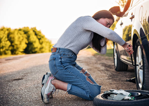 Desperate young woman trying to change a flat tire with tire iron on the road Woman changing wheel after a car breakdown at the side of the road. Transportation, traveling concept. She looks tired and desperate, and waiting help from someone flat tire stock pictures, royalty-free photos & images