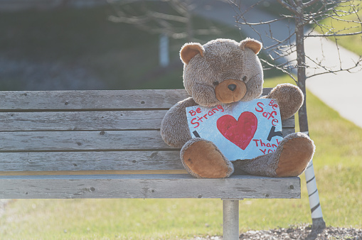 A teddy bear sits on a bench holding a sign of inspiration.
