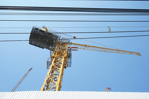 Construction crane and power lines with blue sky background. Low angle shot.