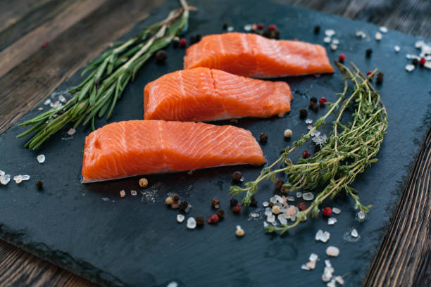istock Three salmon steakes with thyme, rosemary, pepper and salt grains on the black board 1221737993