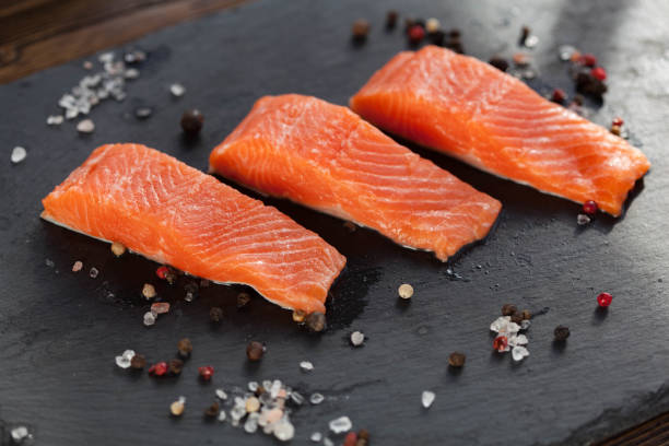 istock Three salmon steakes with pepper and salt grains on the black board 1221737995