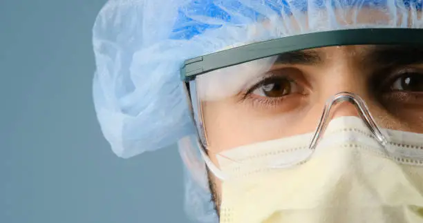 Serious hispanic or middle eastern overworked healthcare worker looking at the camera using a surgical mask and protective eyewear