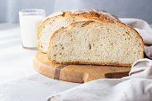 Sliced loaf of freshly baked artisan sourdough bread and a glass of milk. No knead bread. Light grey concrete background.
